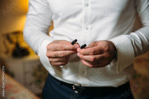 Groom hands hold cufflinks. Elegant gentleman clother, white shirt and black belt