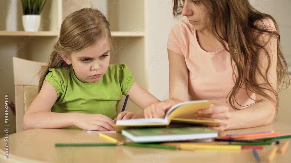 Upset little girl doing school tasks with mother, bored or tired of homework Upset little girl doing school tasks with mother, bored or tired of homework