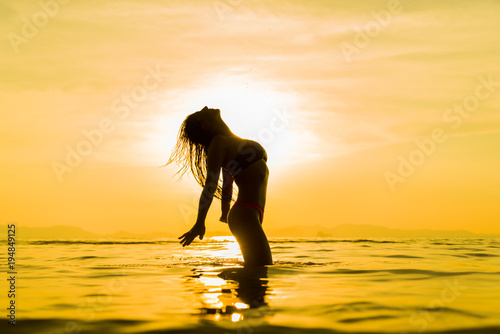 Silhouette of young girl in the water that splashing their hair against sunset © Netfalls