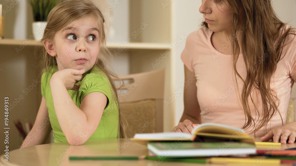 Bored daughter surprisedly looking to mother making her to do homework Bored daughter surprisedly looking to mother making her to do homework