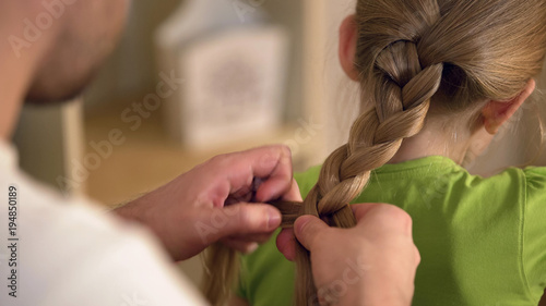 фотографія Father braiding daughters hair carefully, taking care of beloved kid, family