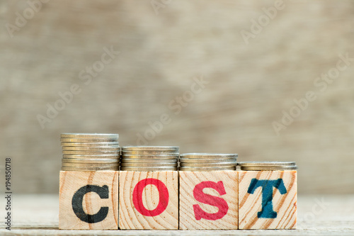 Block in word cost with coin in down trend on wood background