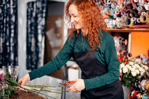 image of pretty girl with red, curly hair making up an attractive bouquet, looking at flowers, taking care of flowers photo