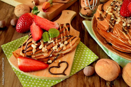 Crepes decorated with nuts, chocolate, fresh strawberries and mint served on a wooden table