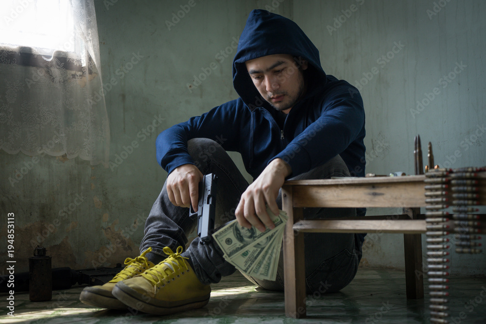 Terrorist sitting in dark and dirty room feeling despair, depressed and sad thinking about bad things. Young hopeless man hands holding gun and money. Drug dealer,criminal with weapons concept. Terrorist sitting in dark and dirty room feeling despair, depressed and sad thinking about bad things. Young hopeless man hands holding gun and money. Drug dealer,criminal with weapons concept.