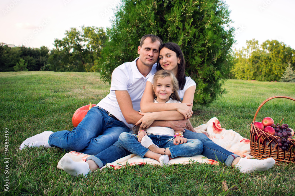 Portrait of a beautiful young happy family at a picnic in the park. Dad hugs his wife and daughter Portrait of a beautiful young happy family at a picnic in the park. Dad hugs his wife and daughter