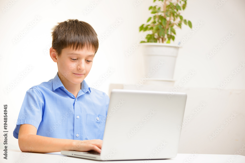 boy in a blue shirt uses a laptop sitting indoors at a table