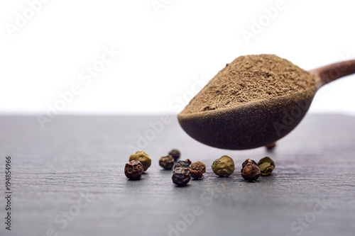 Top view on composition of peppercorns in wooden spoon on dark background, close-up.