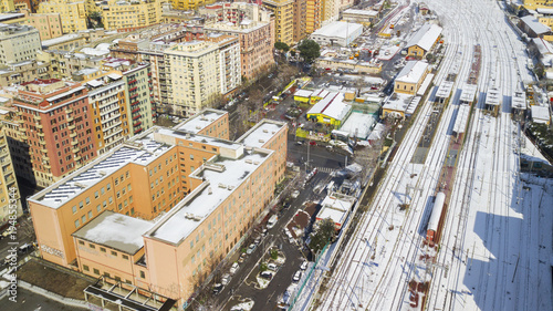 Aerial view of the Tuscolana station in Rome, Italy. Around the tracks there are the palaces and streets of the Italian city. The railroad tracks are made of steel. Everything is covered by snow. © Stefano Tammaro