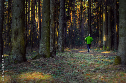 Man trail running in the forest. Morning jogging in the thicket of the forest. Silhouette of an athlete running in the park