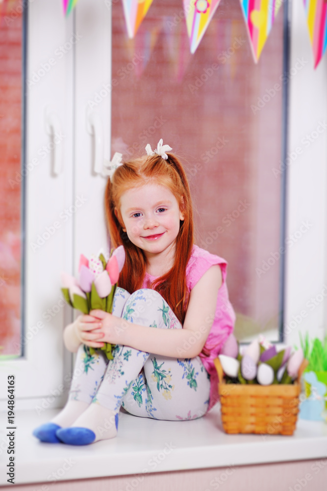 girl with red hair sitting on a windowsill holding a bouquet of tulips in her hands and smiling. March 8, Easter, spring. girl with red hair sitting on a windowsill holding a bouquet of tulips in her hands and smiling. March 8, Easter, spring.