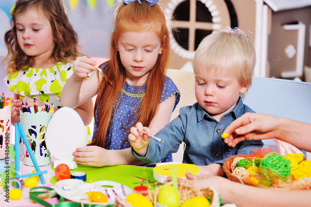 children in kindergarten paint eggs for the Easter basket at the table. children in kindergarten paint eggs for the Easter basket at the table.