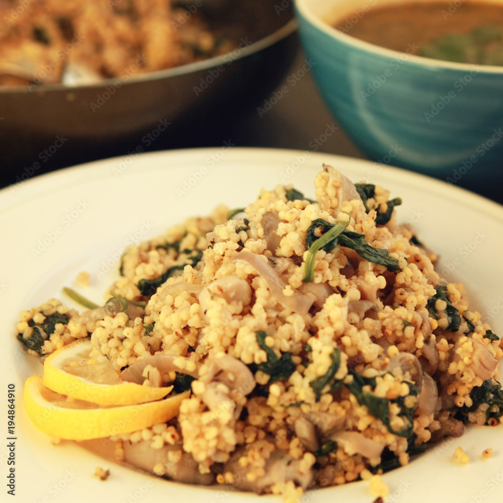 Millet with mushrooms and spinach. Jewish cuisine. Vegetarian couscous on the round white plate. Close up. Toned photo.