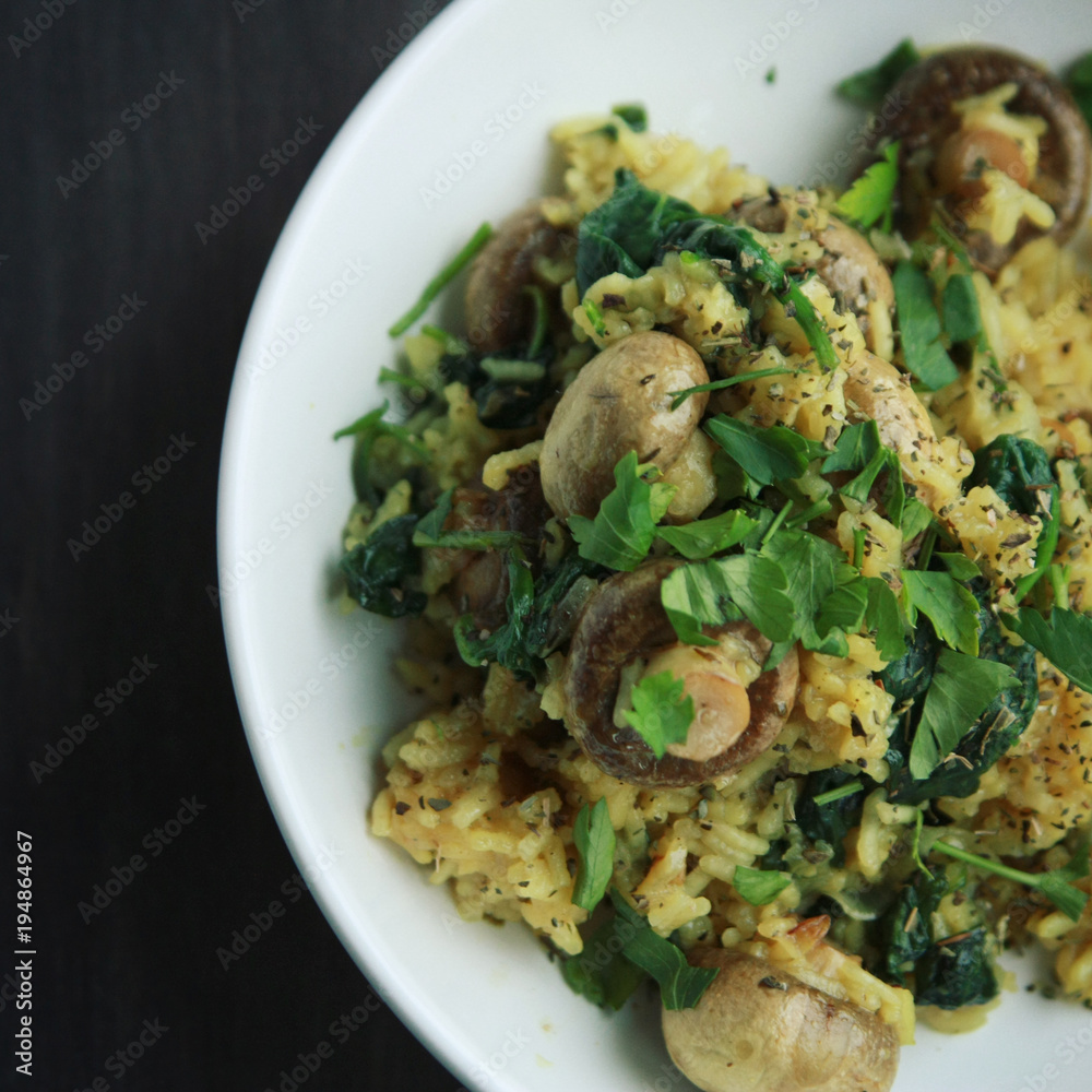 Yellow rice with mushrooms and spinach. Vegan dish. European cuisine. Vegetarian turmeric rice in the white bowl. Close up. Toned image. Yellow rice with mushrooms and spinach. Vegan dish. European cuisine. Vegetarian turmeric rice in the white bowl. Close up. Toned image.