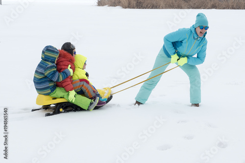 A happy mother with kids in sunglasses and a bright blue ski suit. Mother and children are happy together. A sports family on a snow-covered river with snow. Boys are very happy to play outdoors