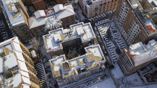 Aerial view of a group of buildings in the residential district of an Italian city. Snow and ice cover the roof of the houses and the square in front of the cars on this cold winter day.