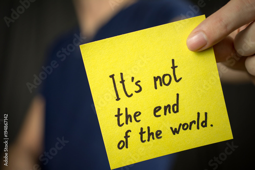 Man holds yellow sticker inscription It's not the end of the world. Blue T-shirt. close-up, selective focus photo