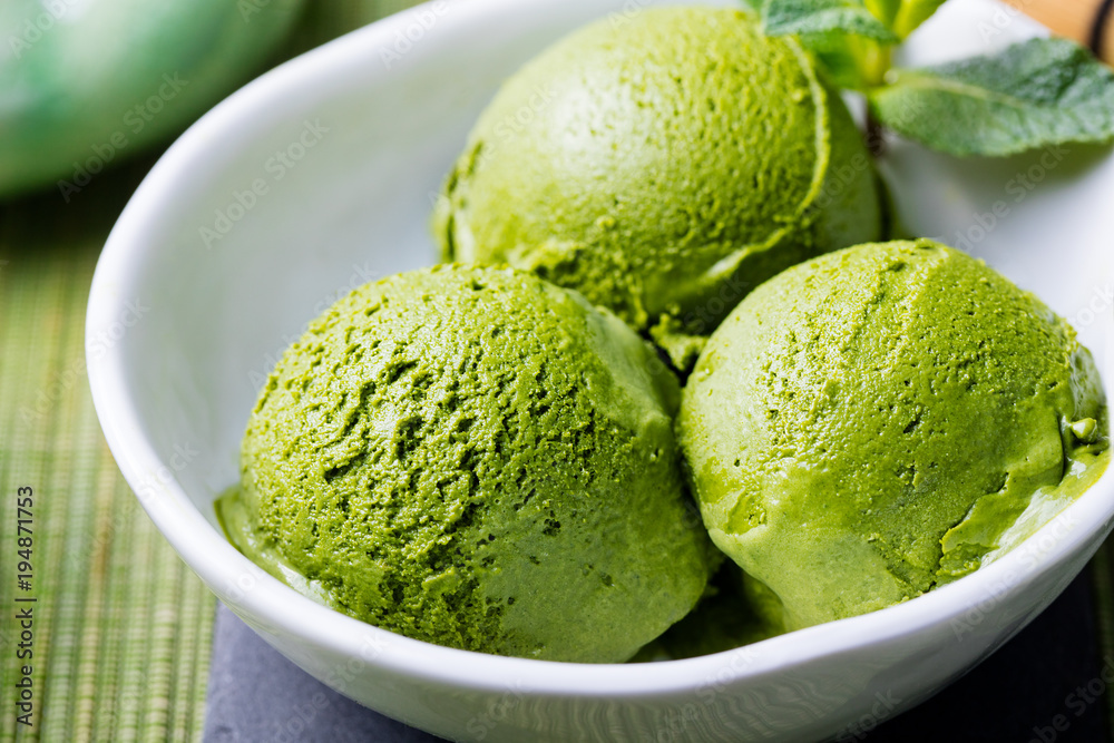 Green tea matcha ice cream scoop in white bowl on a wooden background. Close up. Green tea matcha ice cream scoop in white bowl on a wooden background. Close up.