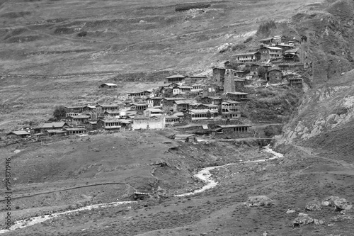 Remote medieval Tushetian village with defencive towers (Dartlo, Georgia). Hills covered with grass. Some huge stones could be seen on the foreground. The river runs down the hill. Black and white. photo