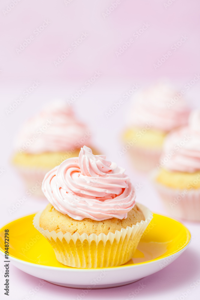 Cupcake decorated with pink buttercream in bright yellow plate on pastel pink background. Sweet beautiful cake. Vertical banner, greeting card, congratulation. Close up photography. Selective focus