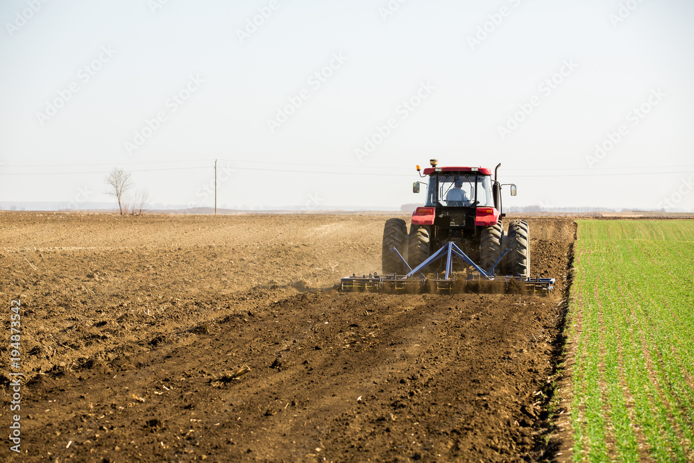 Fototapeta premium Farmer in tractor preparing land with seedbed cultivator as part of pre seeding activities in early spring season of agricultural works at farmlands.