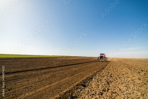 Farmer in tractor preparing land with seedbed cultivator as part of pre seeding activities in early spring season of agricultural works at farmlands.