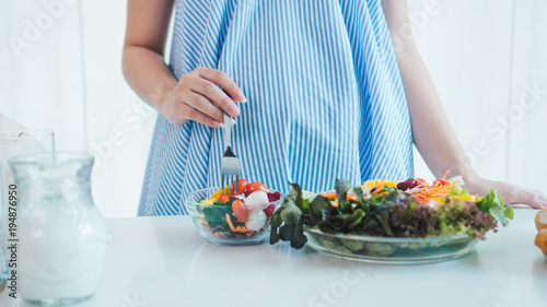 Asian pregnant woman is eating salad.