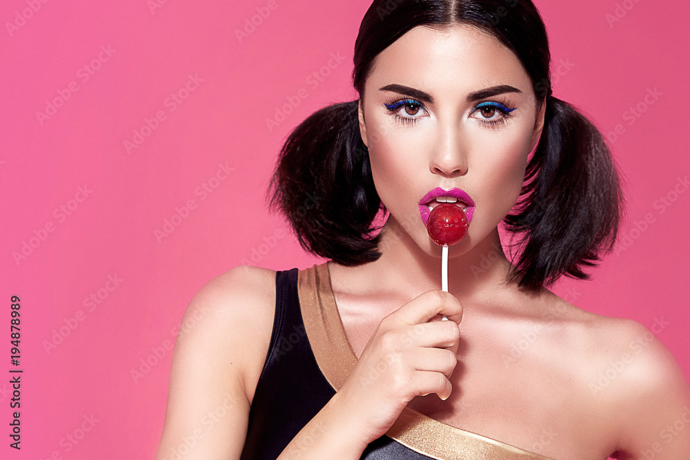 Portrait of sexy beautiful woman brunette hair style perfect bright make up  mascara pink lipstick rouge background face care cosmetic accessory jewelry  eat sweets lollipop candy diet mascara blush. Photos | Adobe