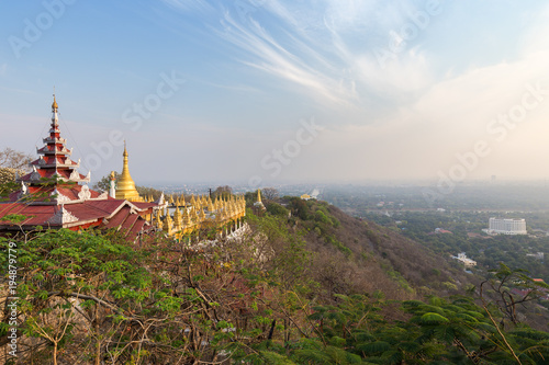Panoramic view of pavilions and golden pagodas at the Mandalay Hill and the city below in Mandalay, Myanmar (Burma) on a sunny day.