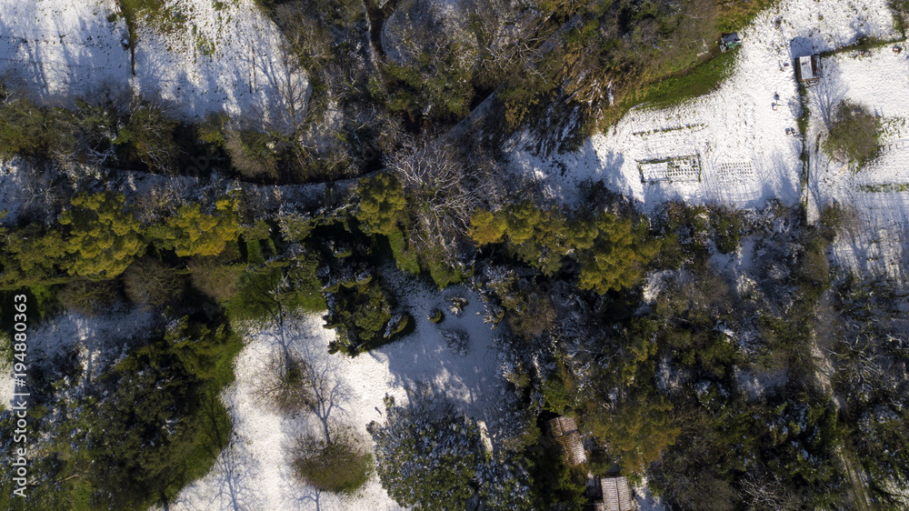 Aerial view of a dirt country road. Around the trees, bushes and grass are covered by snow. Because of the weather there is nobody in this large city park. Aerial view of a dirt country road. Around the trees, bushes and grass are covered by snow. Because of the weather there is nobody in this large city park.