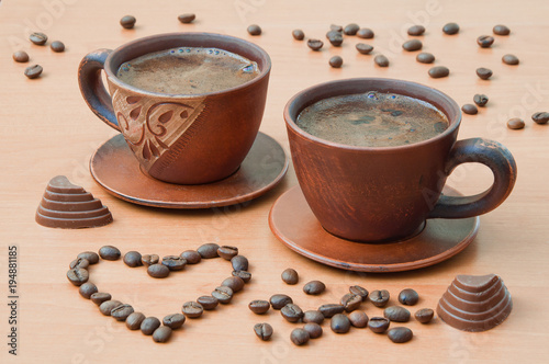 Two cups of coffee with coffee beans in the shape of a heart on a wooden table photo