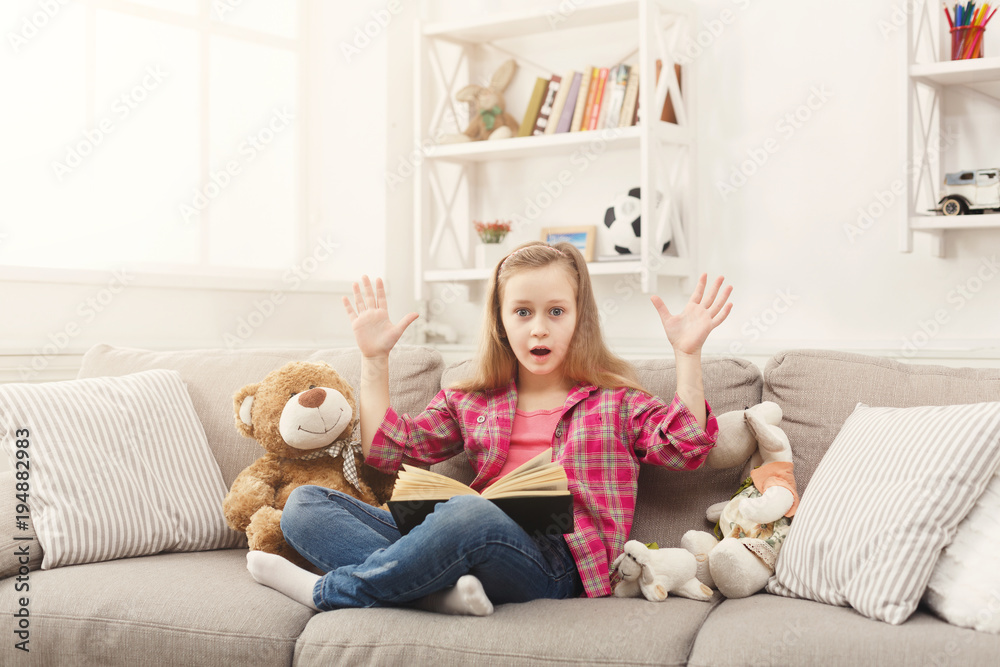 Amazed little girl with book and her favorite toys at home Amazed little girl with book and her favorite toys at home