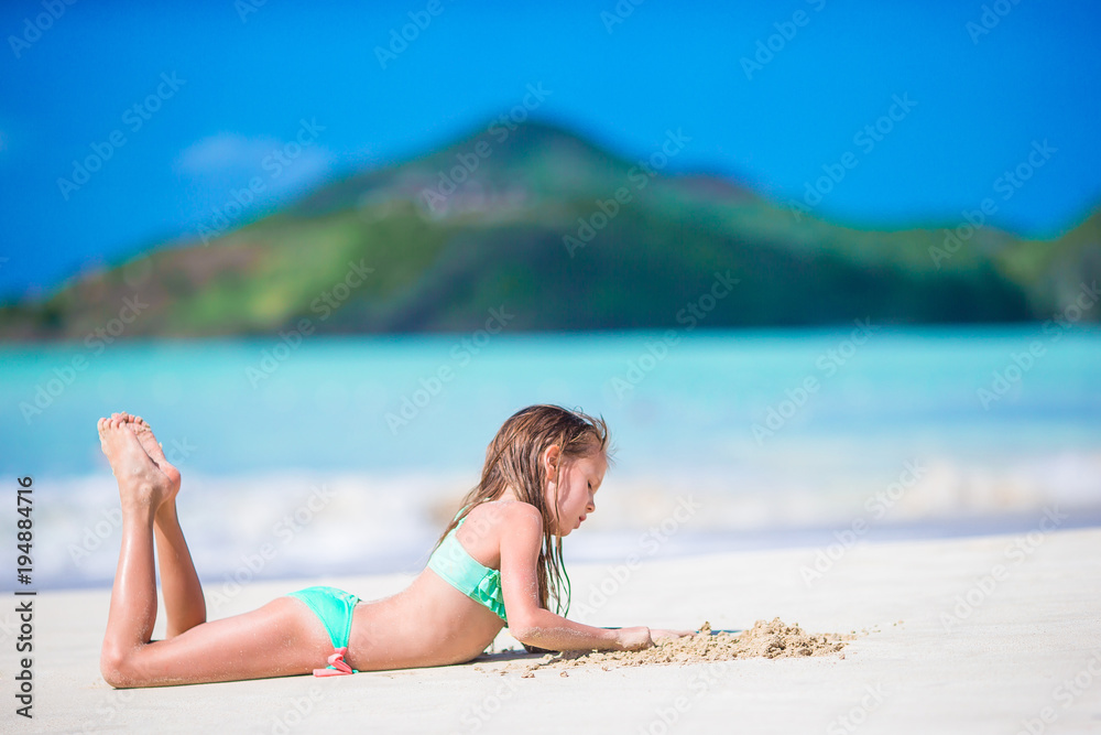Adorable little girl lying on white sandy beach