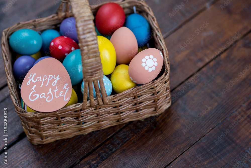 Background image of wicker basket with colorful Easter eggs in on rough wooden table with Happy Easter note Background image of wicker basket with colorful Easter eggs in on rough wooden table with Happy Easter note