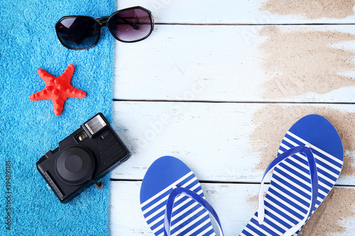 Pair of flip flops with sunglasses, camera and starfish on wooden table