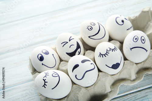 Eggs with funny faces in carton package on wooden table