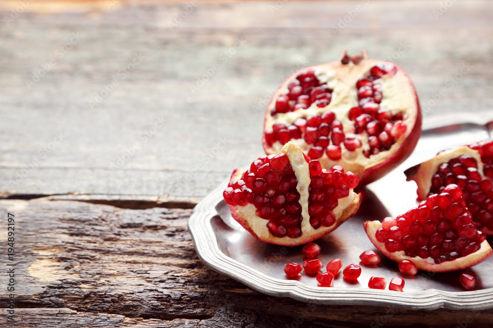 Ripe and juicy pomegranate in tray on grey wooden table Ripe and juicy pomegranate in tray on grey wooden table