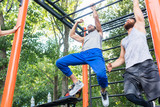 Low-angle view of two strong and competitive men exercising on monkey bars for the upper-body in a modern calisthenics park
