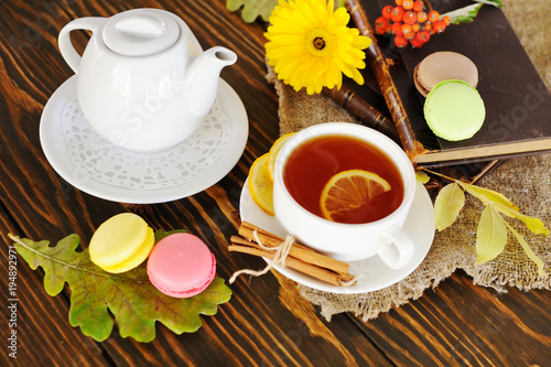 tea with lemon on a wooden background on a background of yellow flowers, colored macaroons, old books and burlap