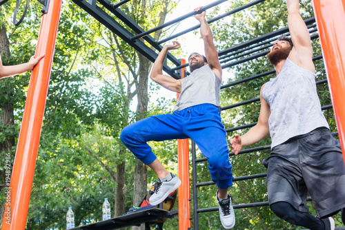Fotografie Low-angle view of two strong and competitive men exercising on monkey bars for t