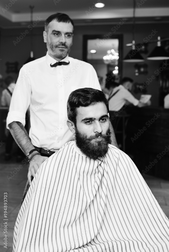 barber does a haircut for a young handsome man with a beard and mustache on the background of Barbashop barber does a haircut for a young handsome man with a beard and mustache on the background of Barbashop
