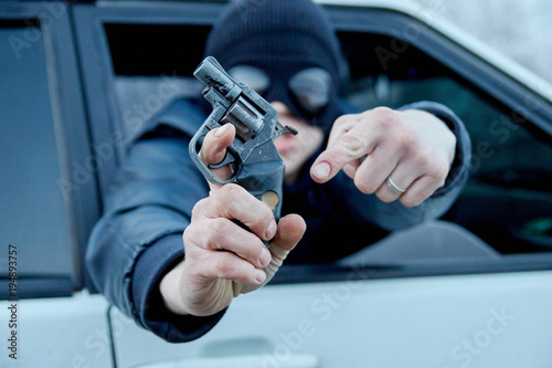 thug in the car on the road with a gun in his hands. robber on the road. a terrorist in a black mask threatens the driver on the road.