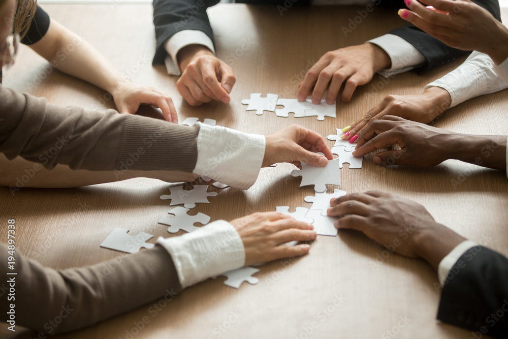 Diverse business people helping in assembling puzzle, cooperation in decision making, team support in solving problems and corporate group teamwork concept, close up view of hands connecting pieces