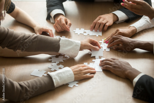 Diverse business people helping in assembling puzzle, cooperation in decision making, team support in solving problems and corporate group teamwork concept, close up view of hands connecting pieces © fizkes