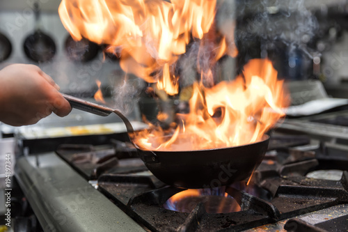 Chef cooking with flame in a frying pan on a kitchen stove.