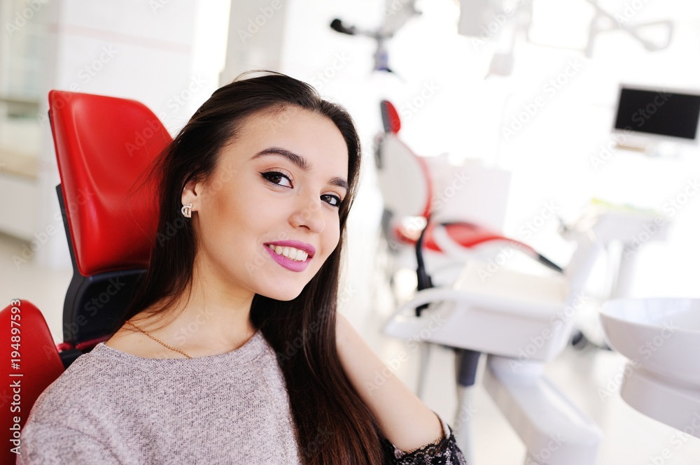 Portrait of a beautiful girl in a red dental chair on the background of a modern clinic Portrait of a beautiful girl in a red dental chair on the background of a modern clinic