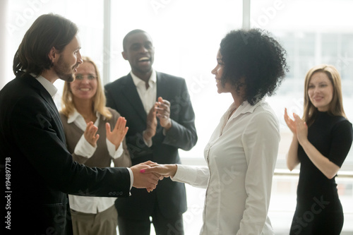 Grateful boss handshaking promoting african businesswoman congratulating with career achievement while colleagues applauding cheering successful worker, appreciation handshake, employee recognition photo