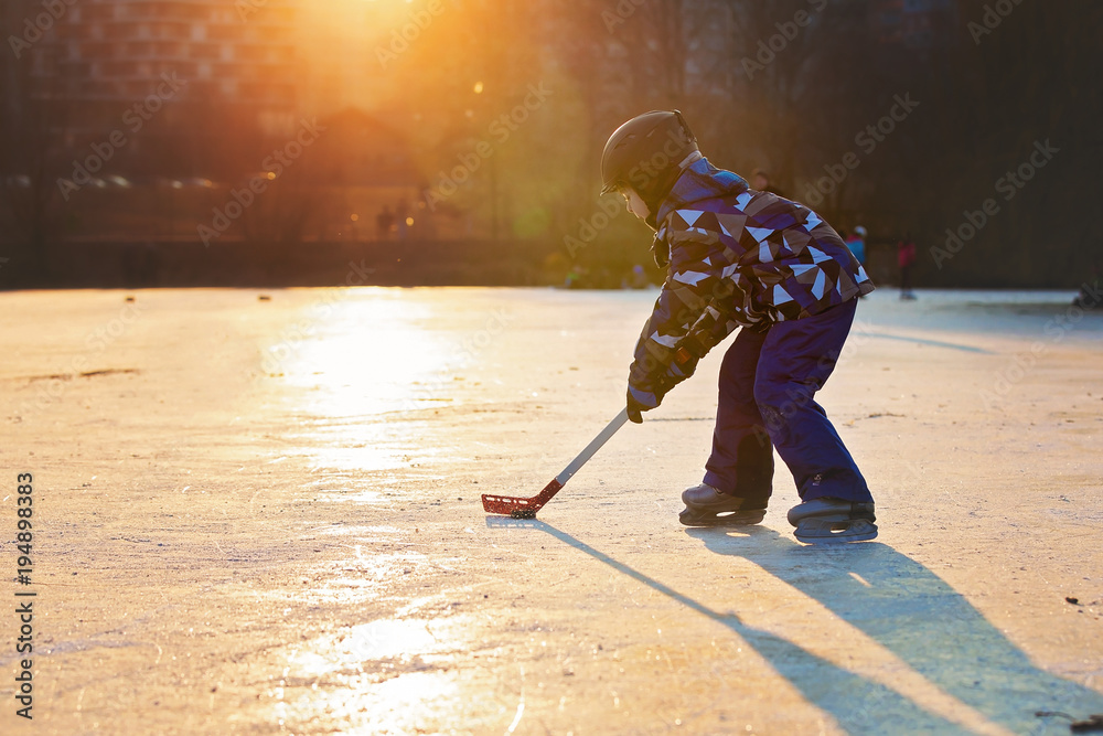 Naklejka premium Children, playing hockey and skating in the park on frozen lake, wintertime on sunset