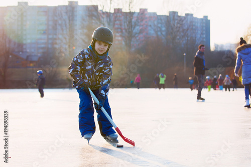 Children, playing hockey and skating in the park on frozen lake, wintertime on sunset