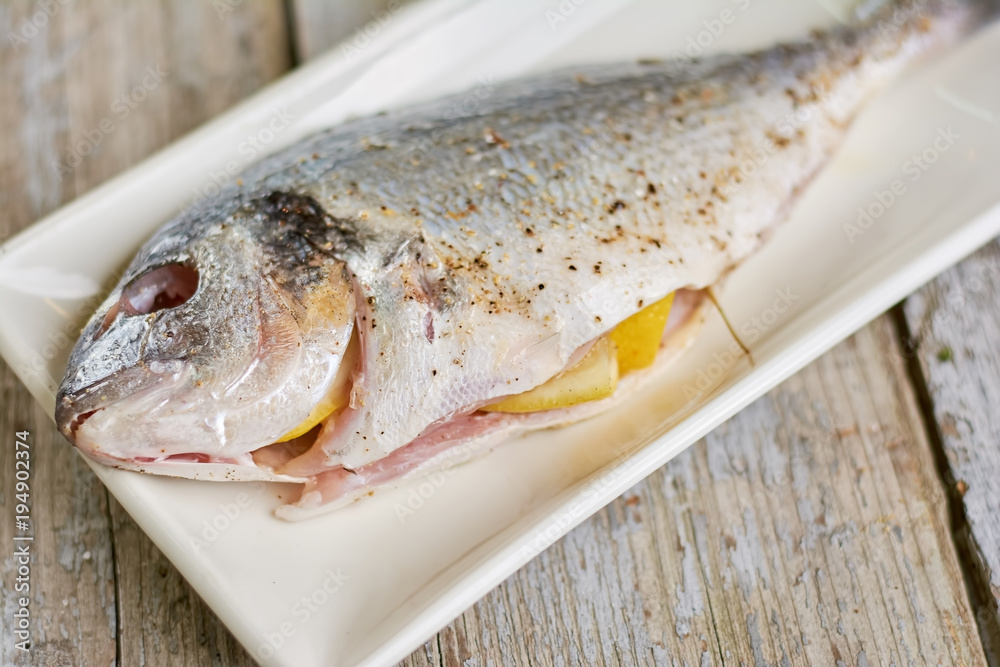 Raw fish with spices and lemons. fresh fih prepared with salt and spices, old wooden background. Recipe of cooking dorado fish at home.